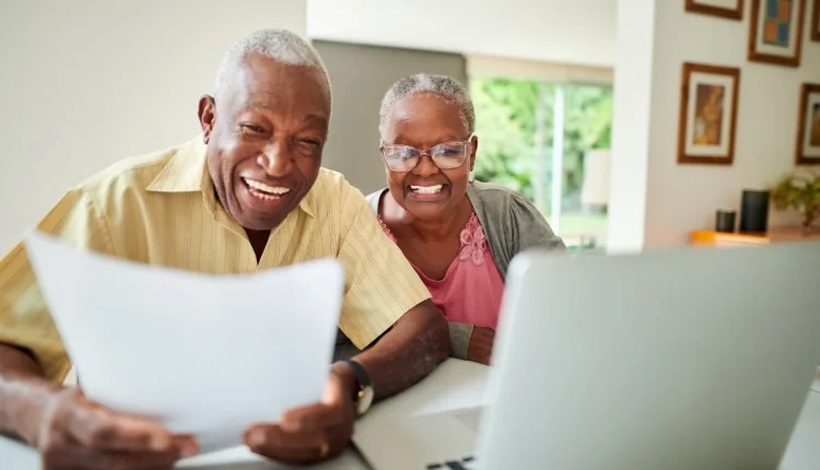 Casal de idosos sorrindo enquanto fazem planejamento financeiro em casa.