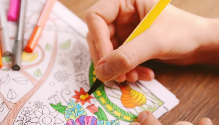Mão de uma pessoa colorindo desenho floral com lápis de cor.