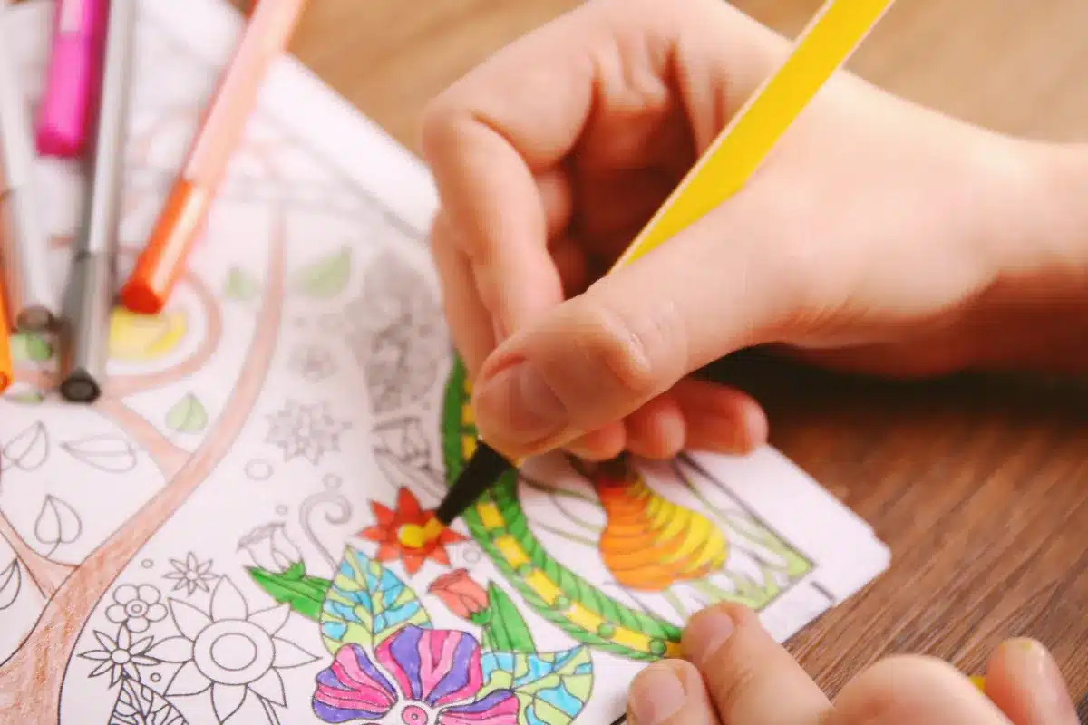 Mão de uma pessoa colorindo desenho floral com lápis de cor.