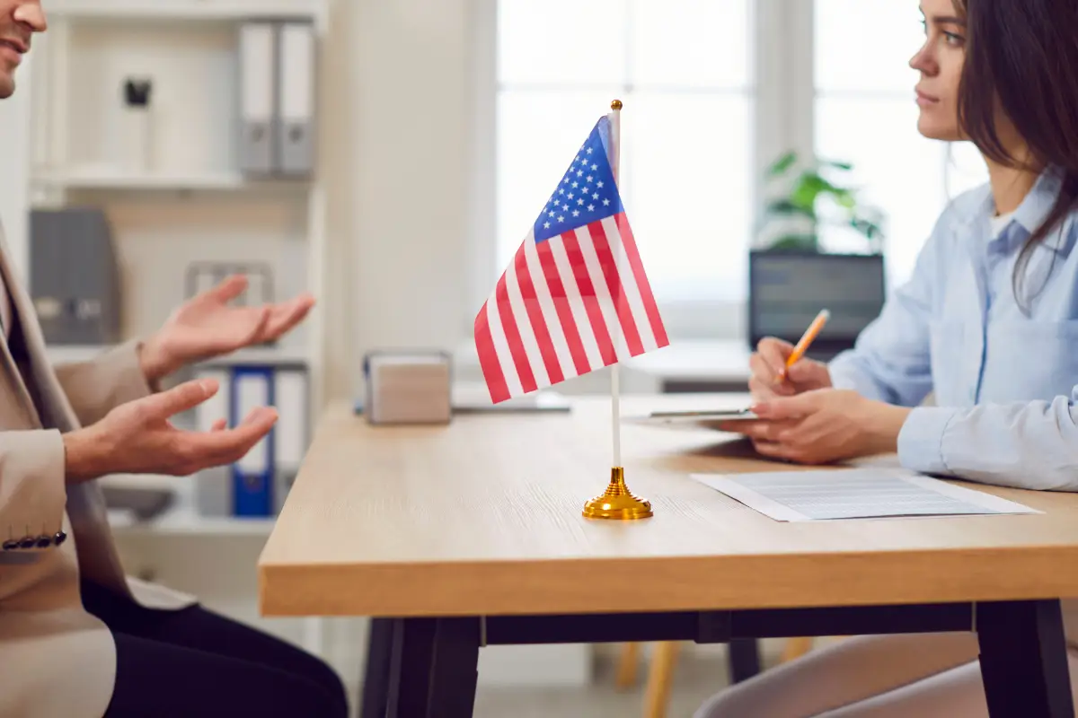Entrevista com bandeira dos Estados Unidos em foco no centro da mesa.