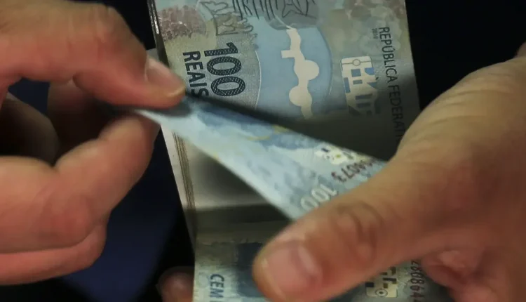 Pessoa contando notas de 100 reais, representando dinheiro em espécie.