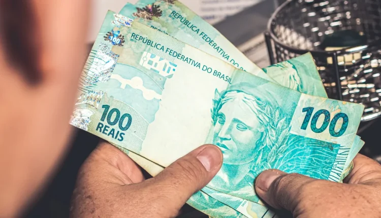 Pessoa segurando várias cédulas de 100 reais em mãos.