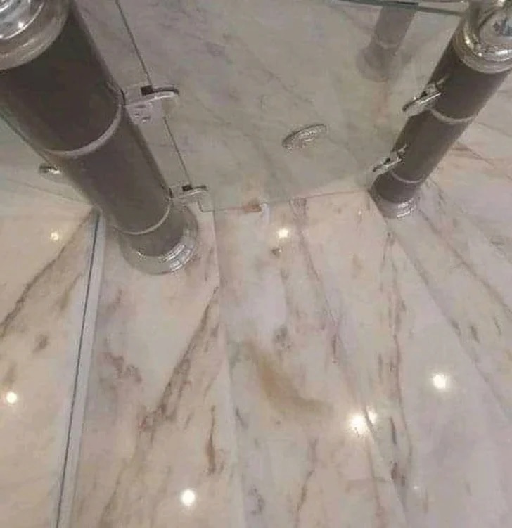 Imagem de piso e paredes de mármore com reflexos e um gato camuflado no canto, quase imperceptível.