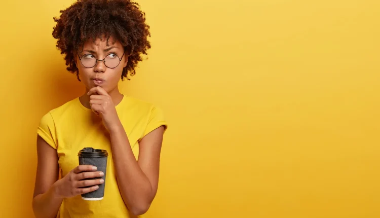 Mulher pensativa com copo de café, questionando o feminino de embaixador