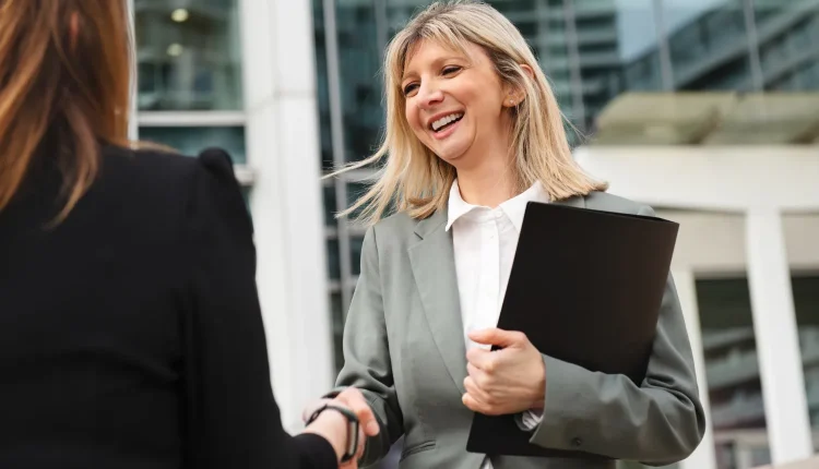 Mulher de negócios sorrindo e cumprimentando outra pessoa, representando um ambiente profissional