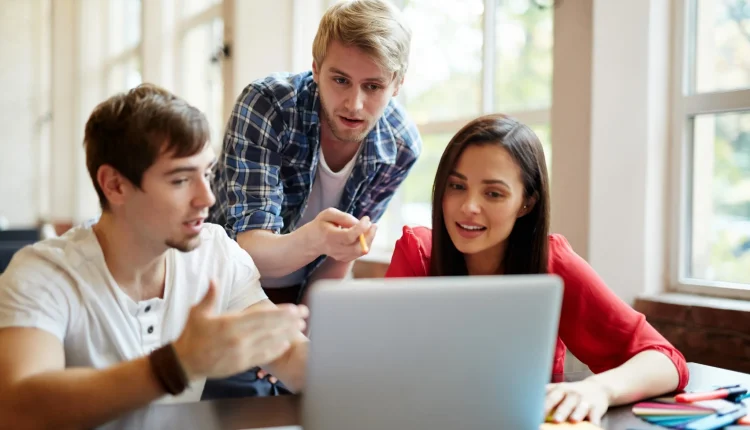 Grupo de jovens profissionais colaborando em projeto usando notebook.
