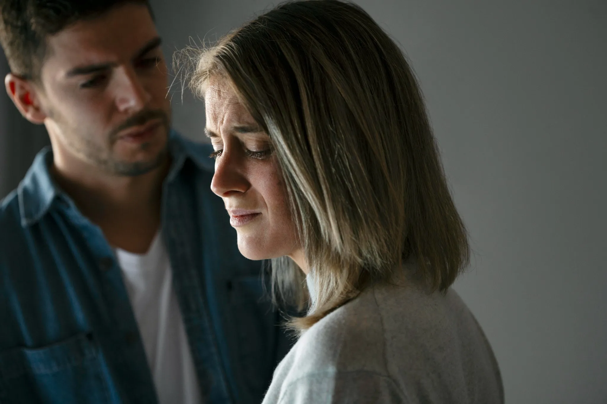 Mulher com expressão de angústia enquanto recebe o apoio de um homem, em um momento emocionalmente intenso.