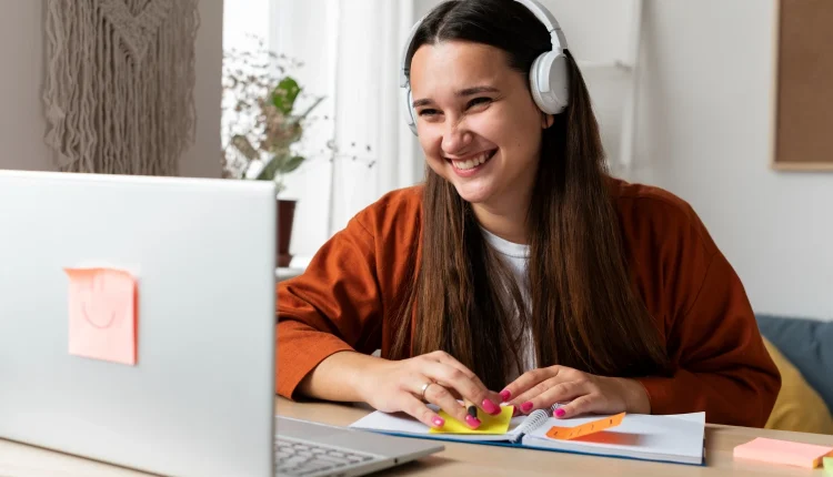 Jovem mulher sorridente com fones de ouvido estudando online com notebook e cadernocertificado reconhecido pelo mec
