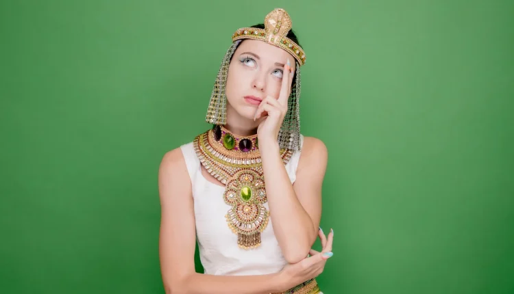 Mulher vestida com traje egípcio antigo, com expressão pensativa, imitando a aparência de Cleópatra.