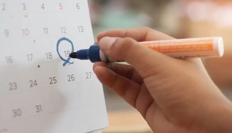 Mão marcando uma data no calendário com marcador azul