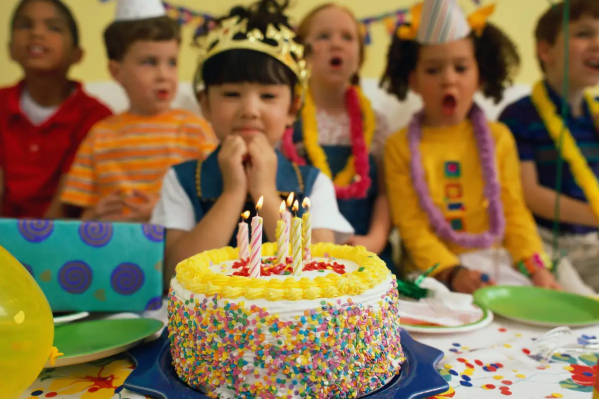 Crianças comemorando aniversário com bolo decorado e velas acesas.