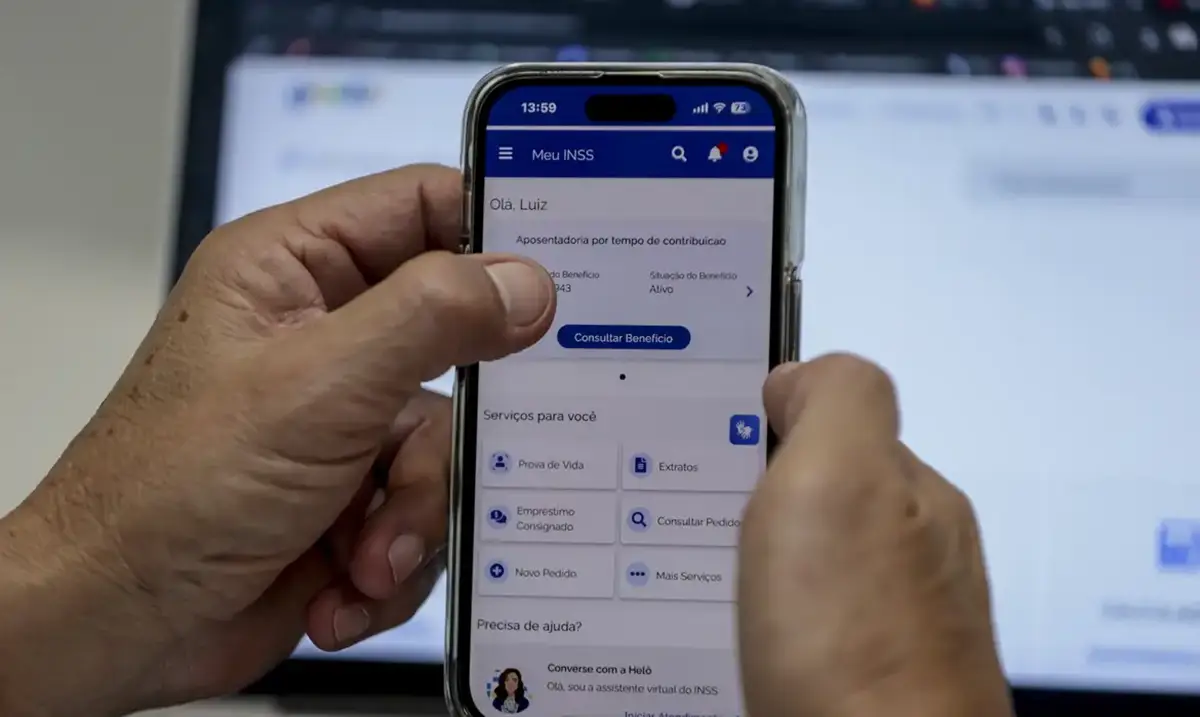 Mãos segurando um smartphone com a tela do aplicativo Meu INSS mostrando opções de serviços.