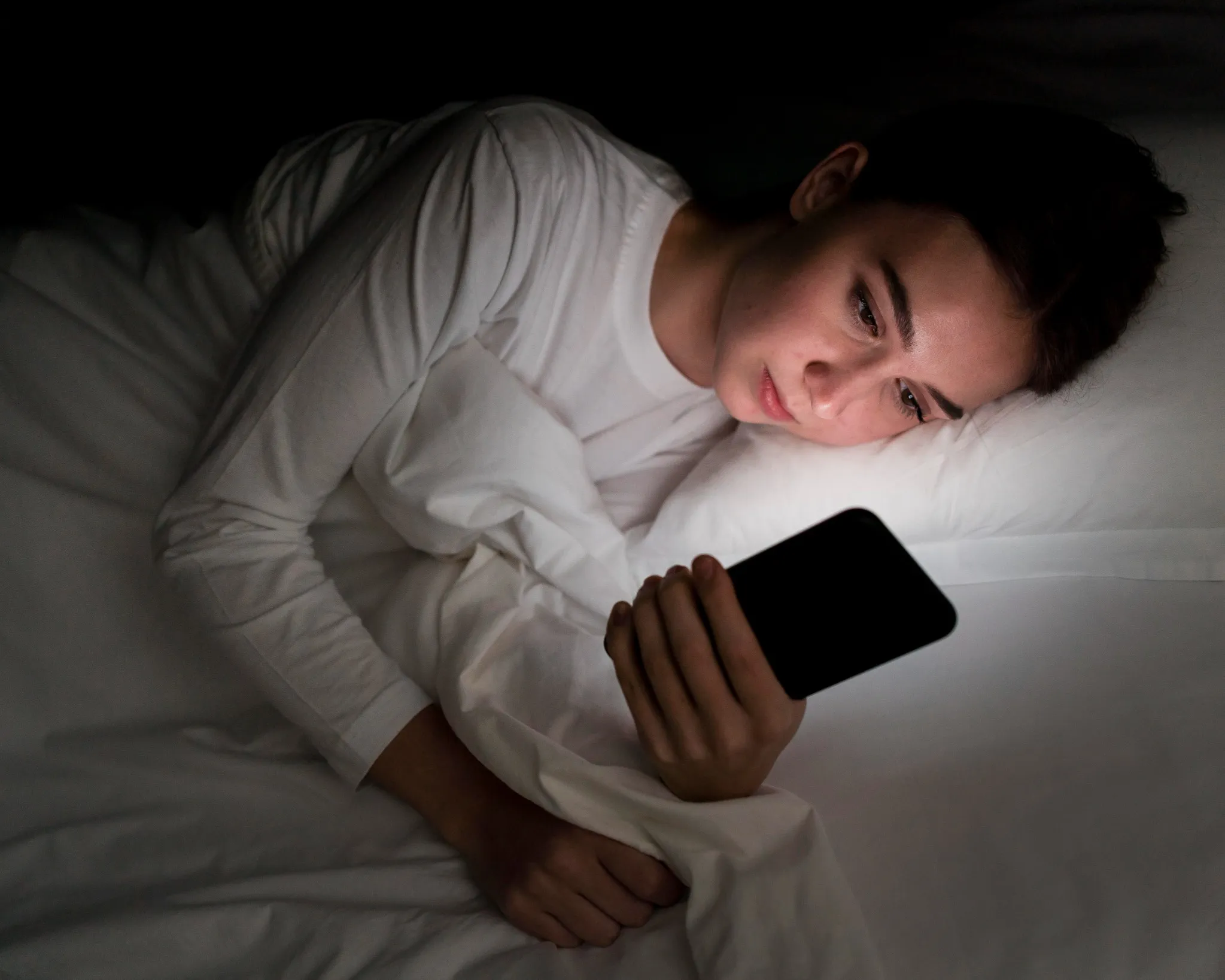 Jovem mulher deitada na cama à noite olhando para a tela do celular