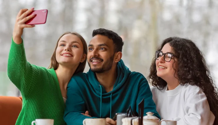 Três amigos sorrindo enquanto tiram uma selfie em um café, refletindo amizade e interação social