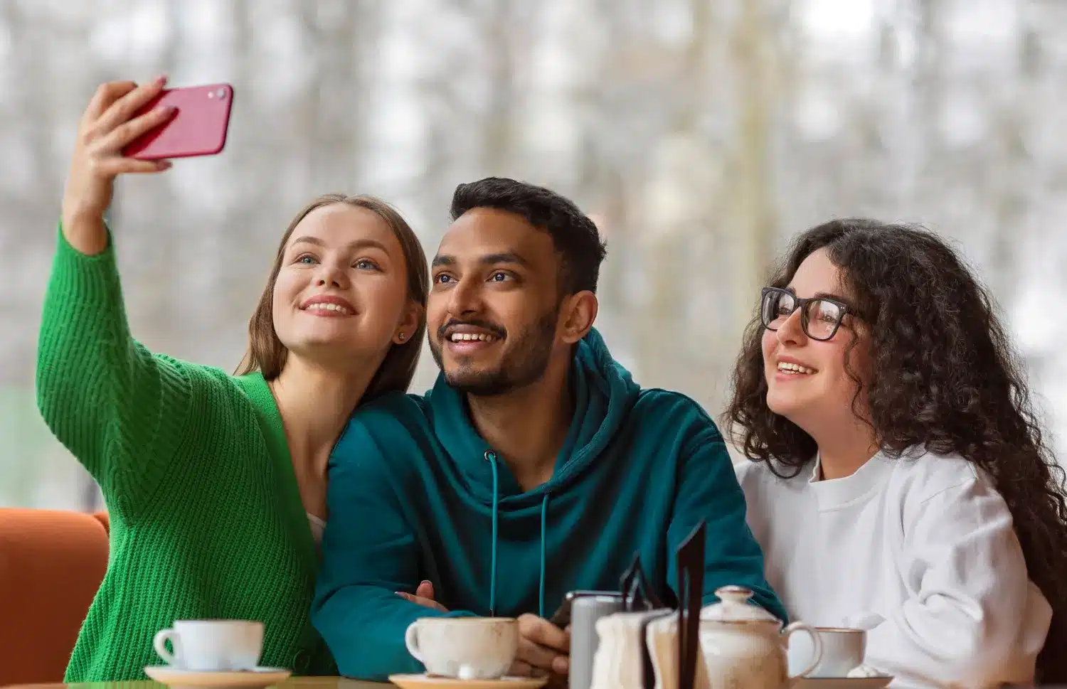 Três amigos sorrindo enquanto tiram uma selfie em um café, refletindo amizade e interação social