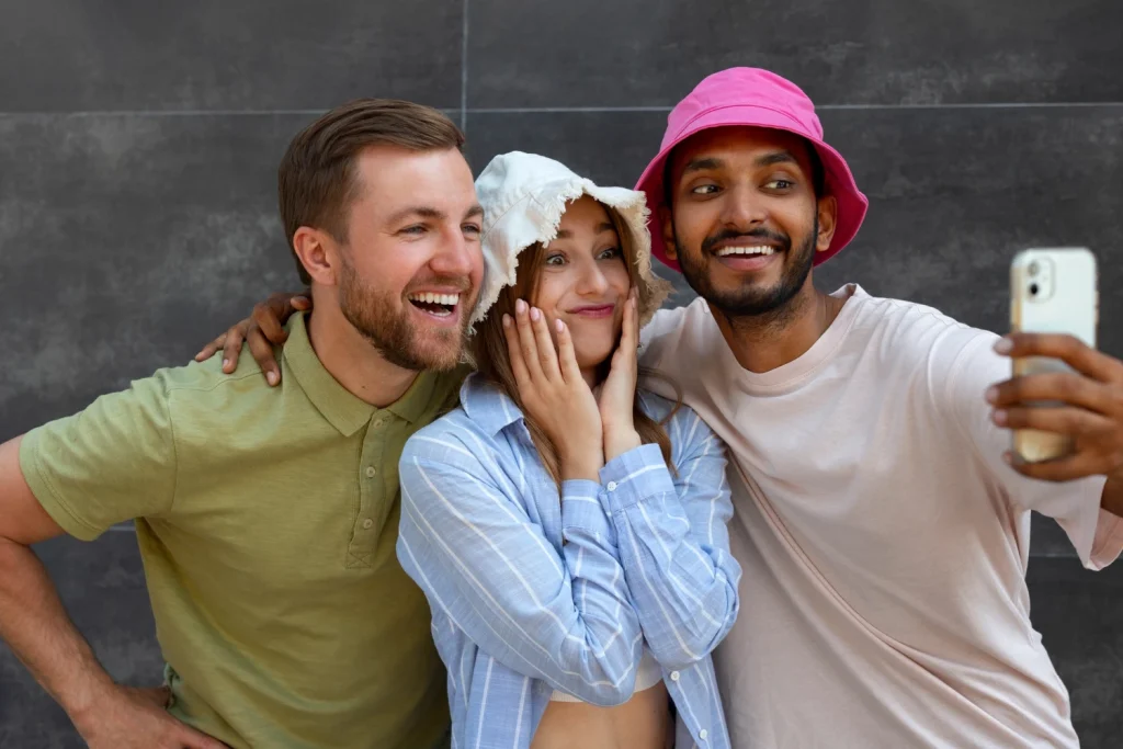 Três amigos animados tirando selfie, mostrando diferentes expressões e alegria em um momento social