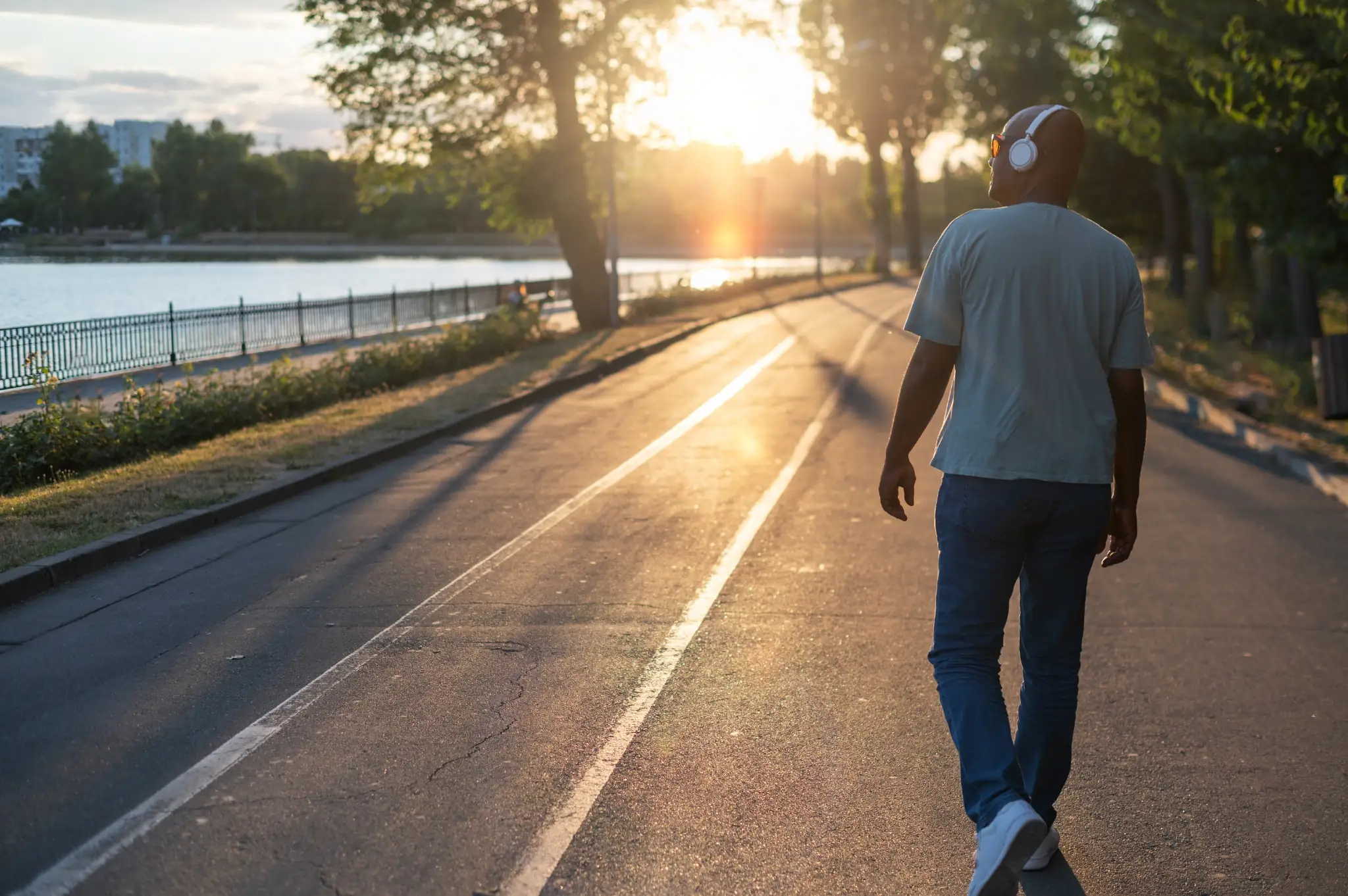 Homem caminhando ao pôr do sol ouvindo música com fones de ouvido brancos.