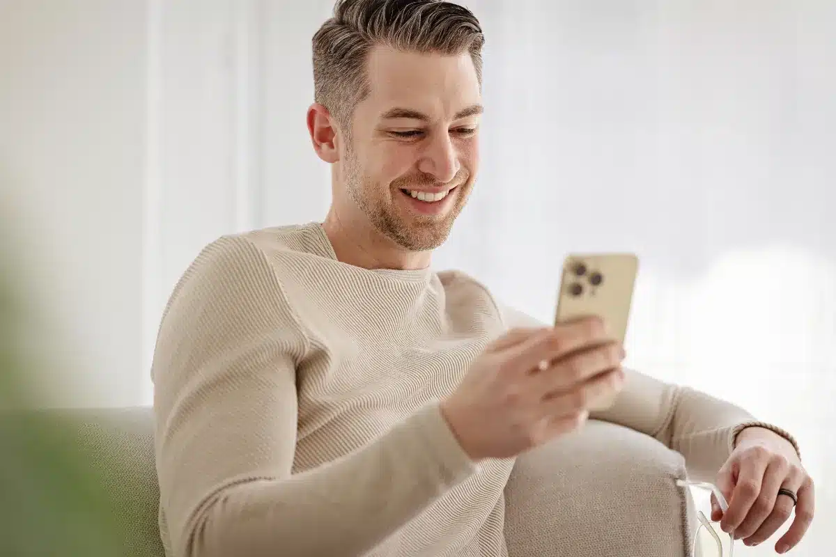 Homem sorrindo enquanto confere mensagens no celular.