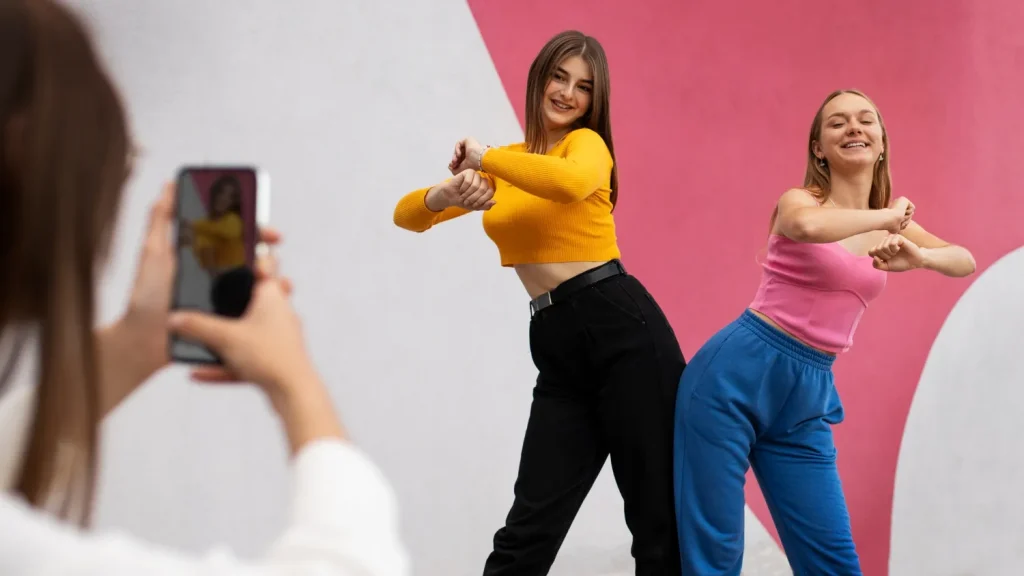 Duas jovens fazendo pose de dança para um vídeo, enquanto uma terceira pessoa grava com um celular, representando criadores de conteúdo digital no TikTok