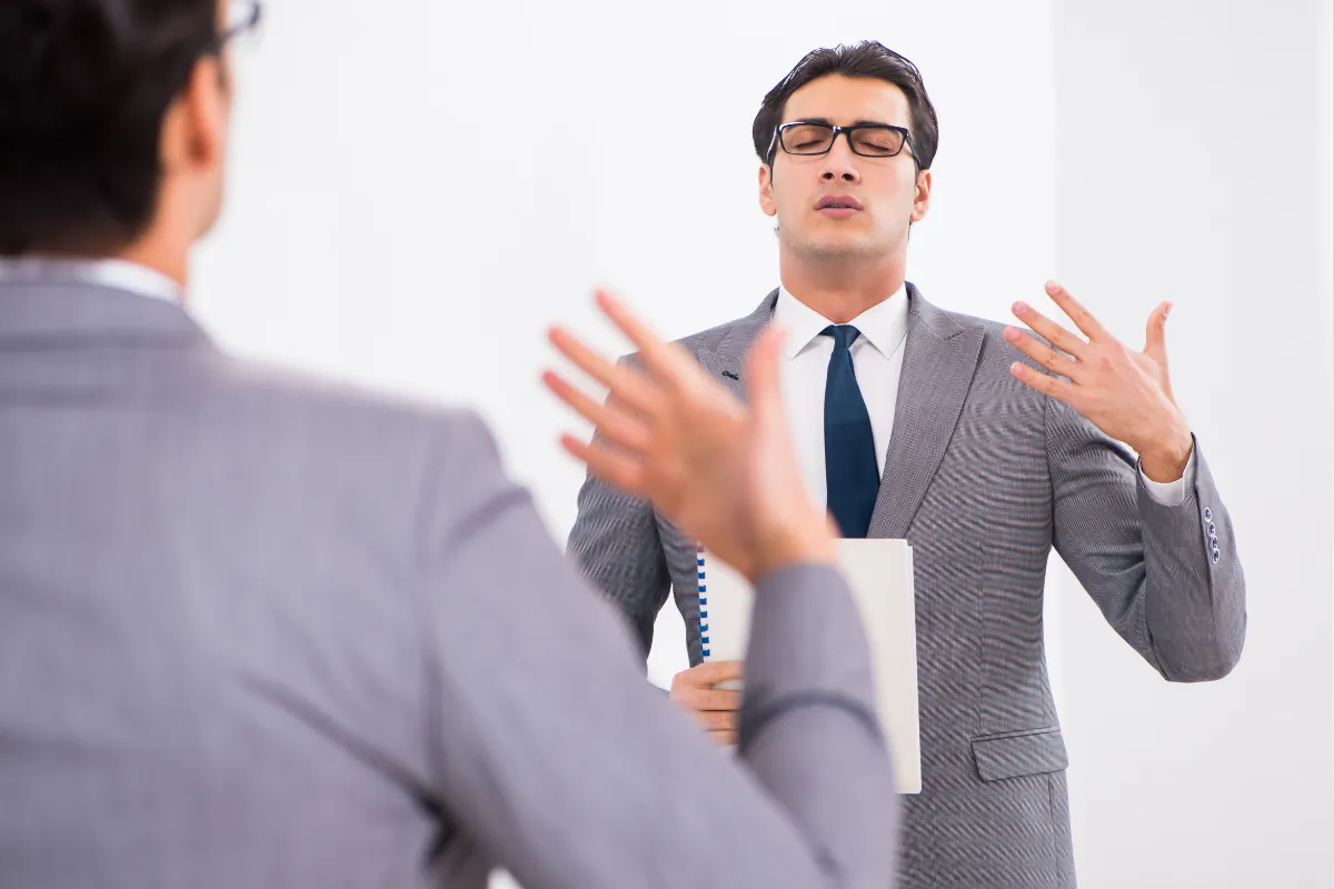 Homem de terno praticando linguagem corporal em frente ao espelho com olhos fechados.
