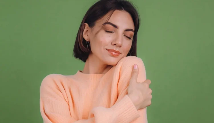 Mulher sorrindo e abraçando a si mesma, simbolizando o cuidado com a autoestima.