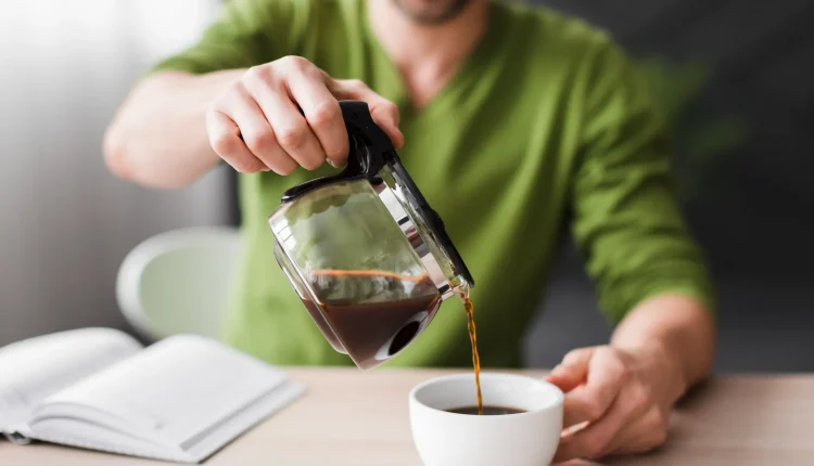 Homem sorridente servindo café fresco em uma xícara branca sobre a mesa.
