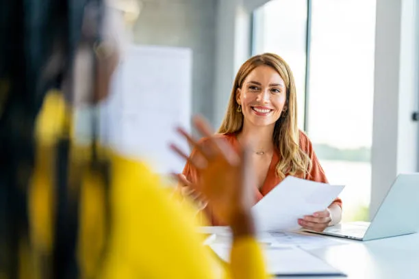 Mulher sorridente segurando papéis durante entrevista de emprego em ambiente de escritório moderno