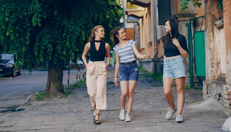 Três amigas caminhando em uma rua de paralelepípedos, conversando e sorrindo, representando traços de personalidade pelo jeito de andar.