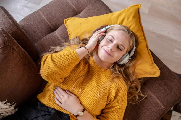 Mulher deitada no sofá ouvindo música com fones e expressão relaxada