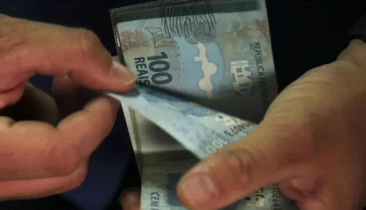 Pessoa contando cédulas de 100 reais, representando o pagamento do 13º salário do INSS para os novos grupos
