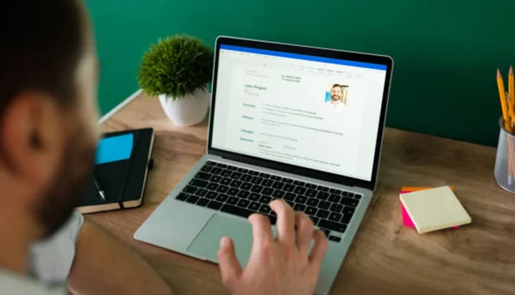 Homem digitando em laptop com currículo aberto na tela, simbolizando otimização de currículos para sistemas de recrutamento automatizados
