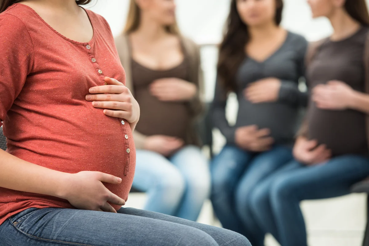 Grupo de mulheres grávidas sentadas, com as mãos na barriga, em um ambiente tranquilo.
