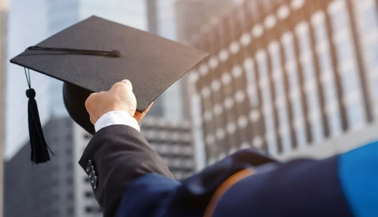 Pessoa segurando capelo de formatura em frente a prédios modernos, celebrando a conquista acadêmica