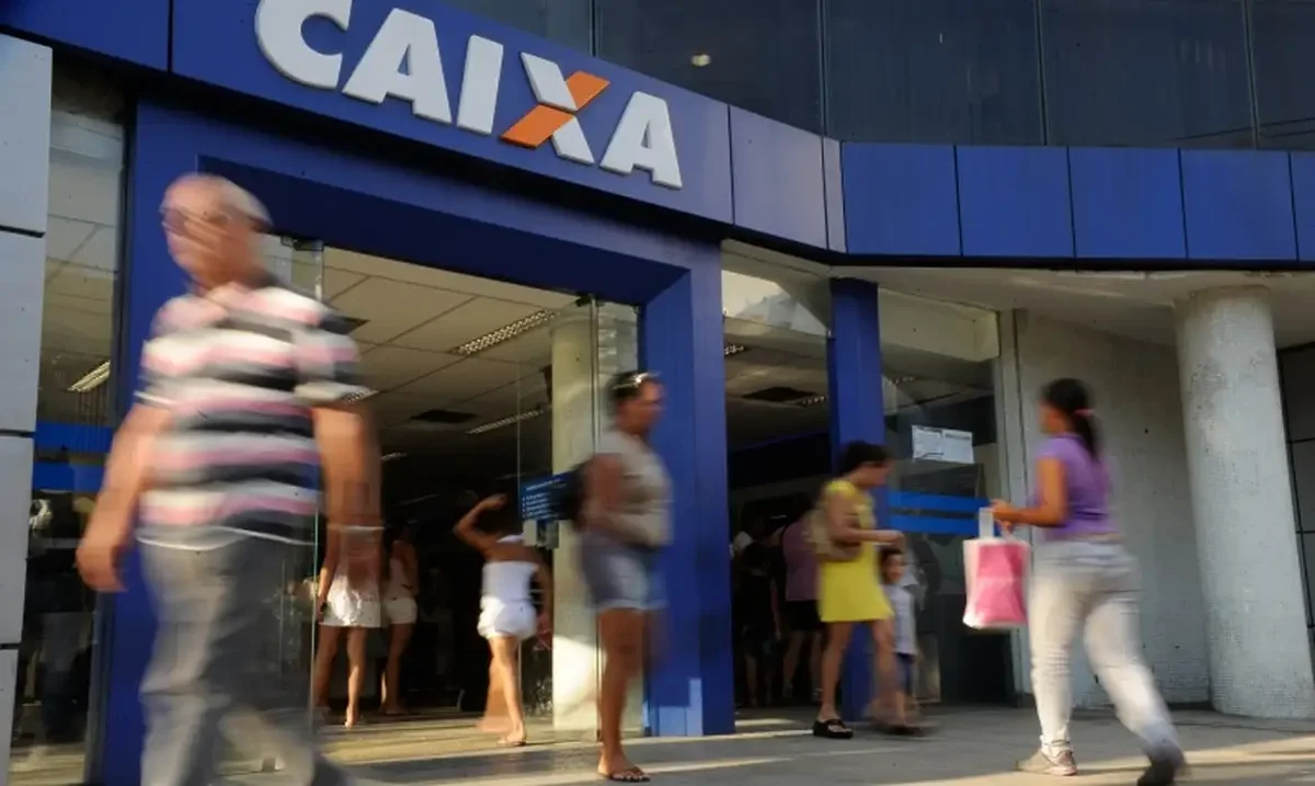 Pessoas caminhando na entrada de uma agência da Caixa Econômica Federal.