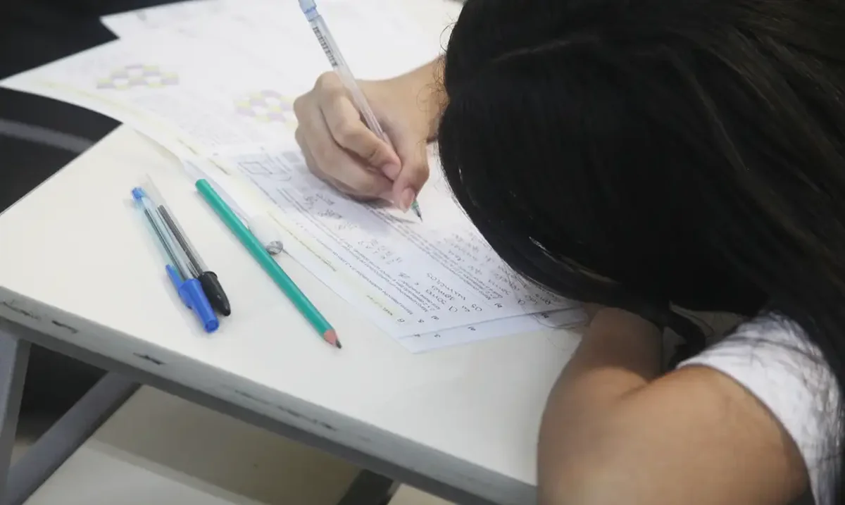 Estudante escrevendo uma redação, com foco na organização e estruturação de conteúdo no processo de aprendizado.