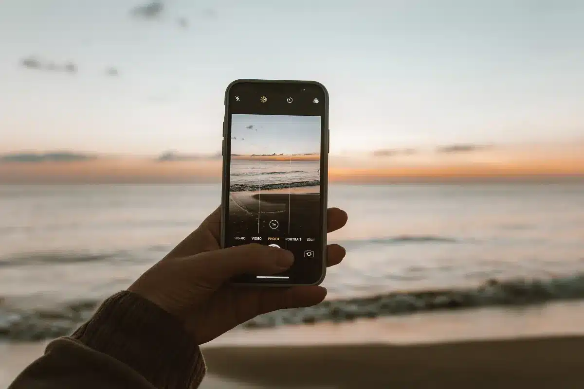 Pessoa registra o pôr do sol na praia usando o celular.