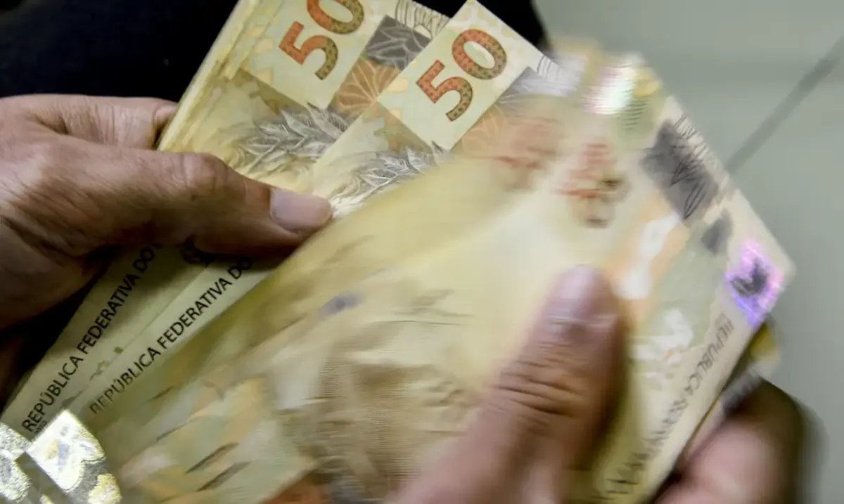 Pessoa segurando cédulas de 50 e 100 reais, simbolizando os beneficiários da nova tabela do Imposto de Renda