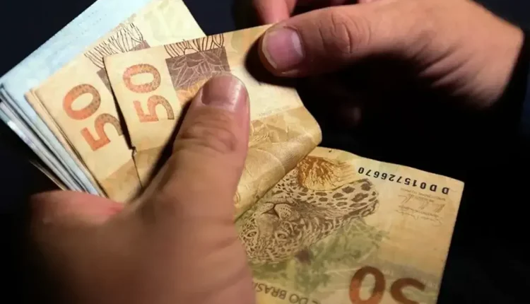 Pessoa contando cédulas de 50 reais, simbolizando o pagamento do 13º salário do INSS