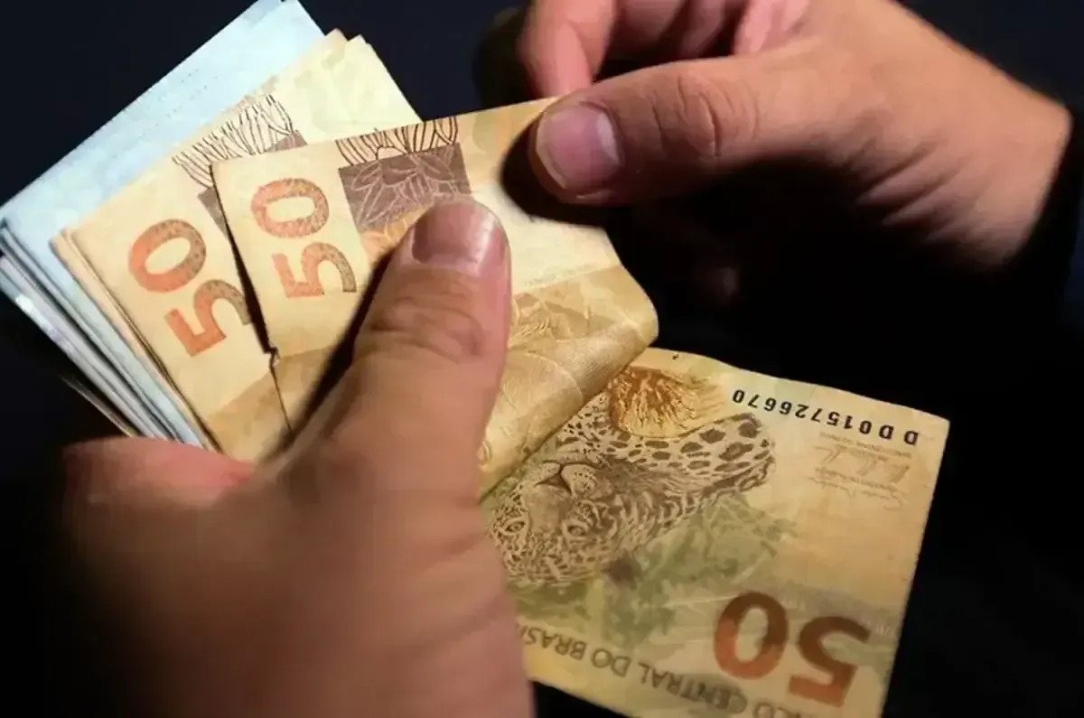 Pessoa contando cédulas de 50 reais, representando o valor do pagamento do programa Pé-de-Meia para Licenciaturas.