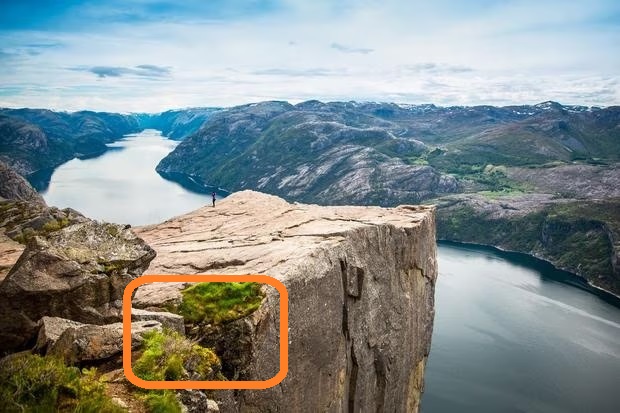 Solução do teste de QI com pessoa em pé na beira de um penhasco com vista para um fiorde rodeado por montanhas e água.