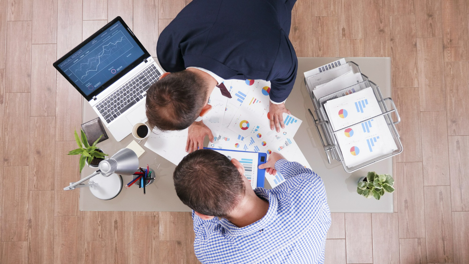 Duas pessoas analisando gráficos financeiros e relatórios em mesa de escritório moderno.