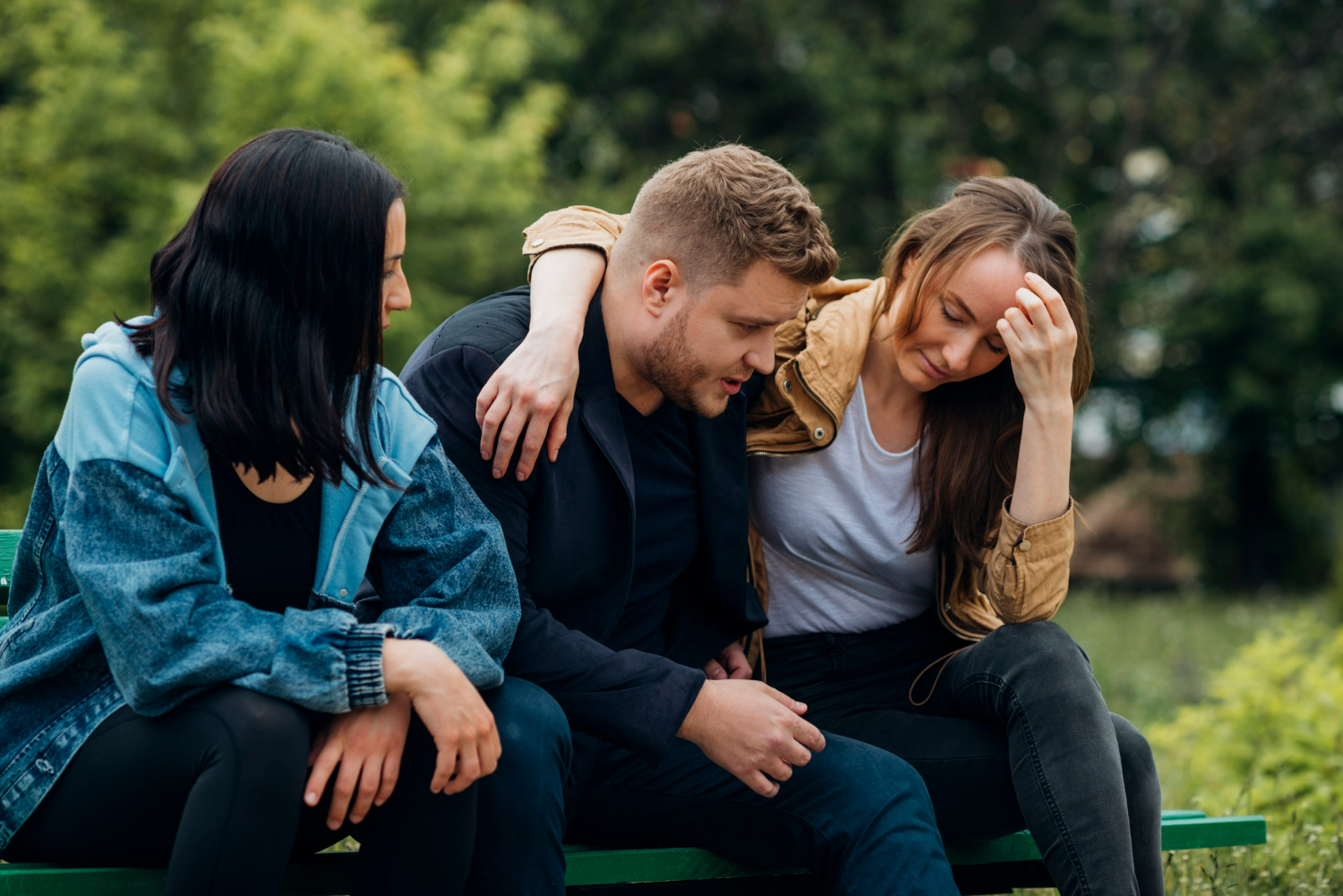 Grupo de amigos em banco de parque, com uma pessoa consolando outra.