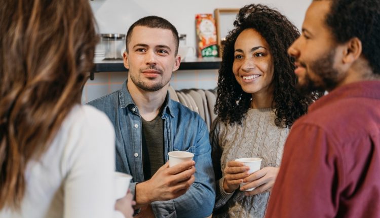 Grupo de pessoas sorrindo e conversando com xícaras de café em mãos.