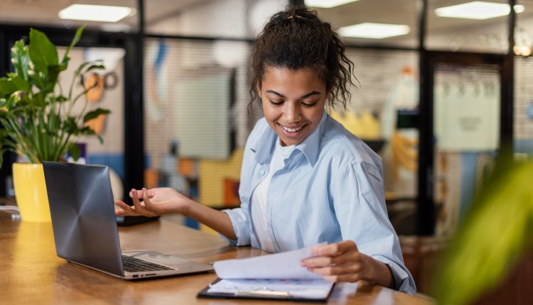 Jovem sentada à mesa, com caderno, caneta e laptop, estudando para cursos técnicos.