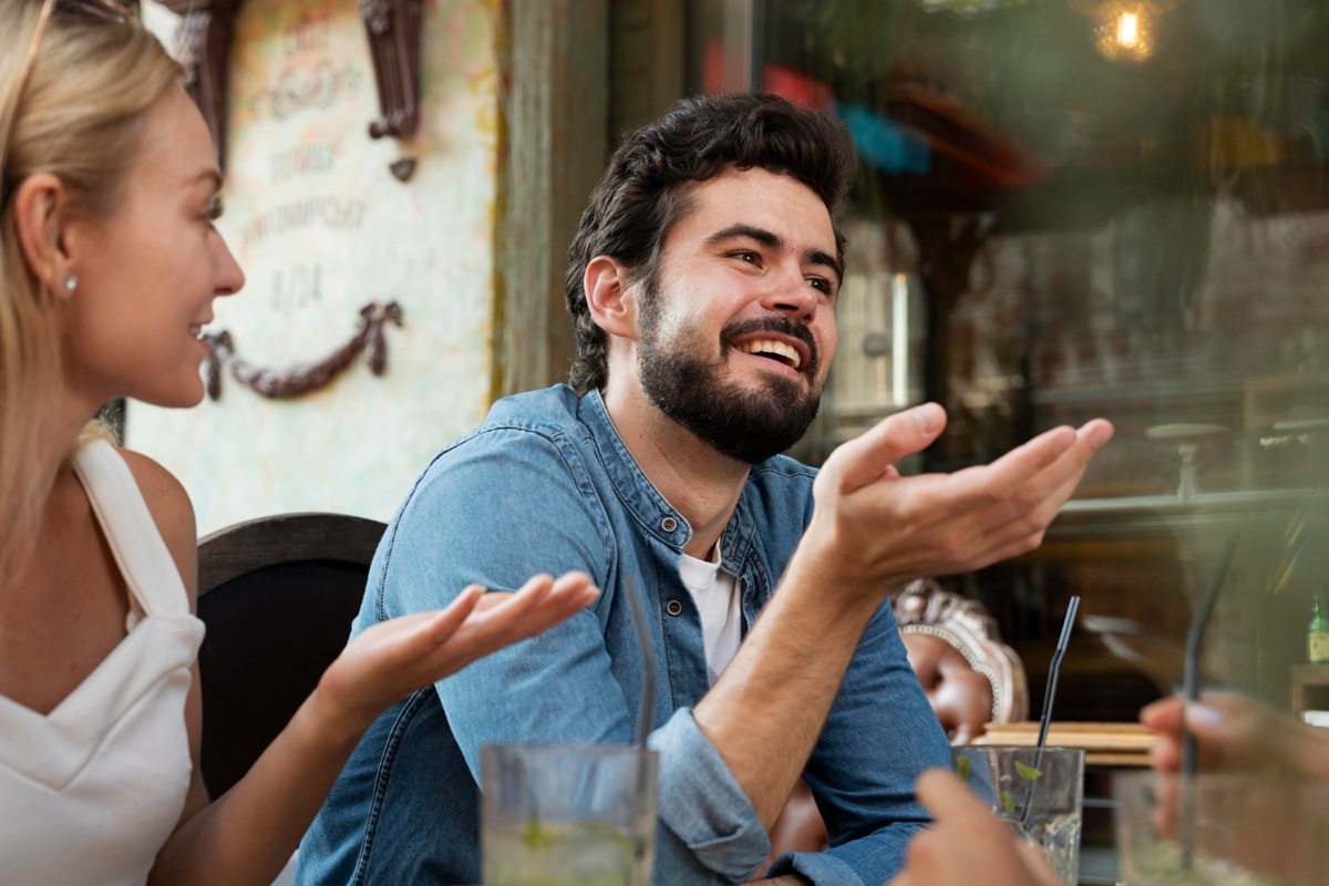 Homem sorrindo enquanto conversa com mulher em ambiente social.