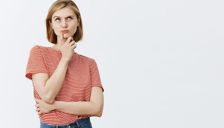 Jovem com camisa listrada vermelha e branca, pensativa com a mão no queixo.