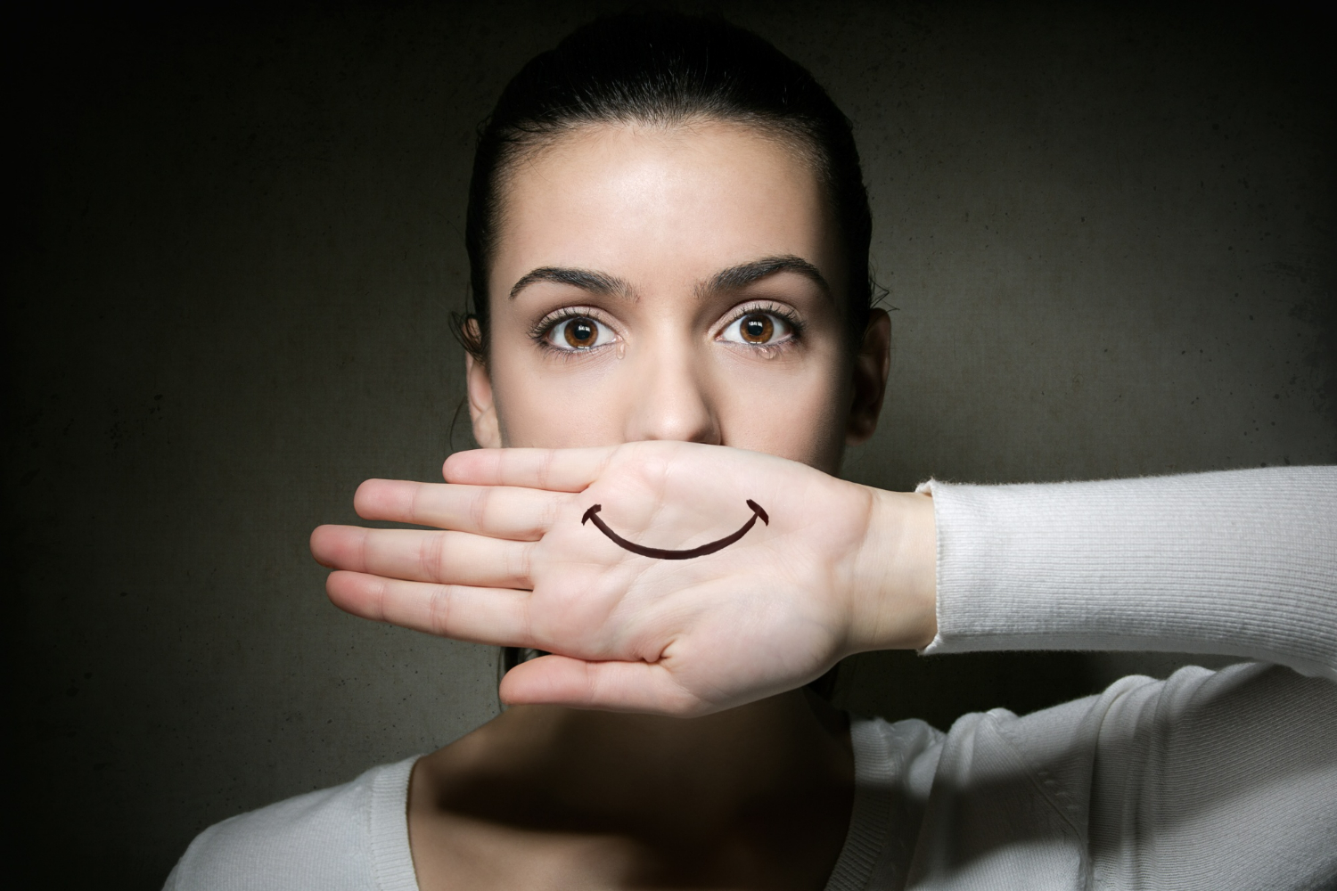 Mulher com expressão neutra cobrindo a boca com a mão, simbolizando a dificuldade em expressar ou identificar emoções.