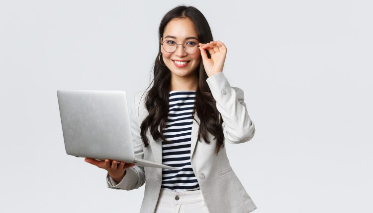 Mulher sorrindo enquanto segura um laptop, ajustando seus óculos, representando profissionalismo e autoconfiança.
