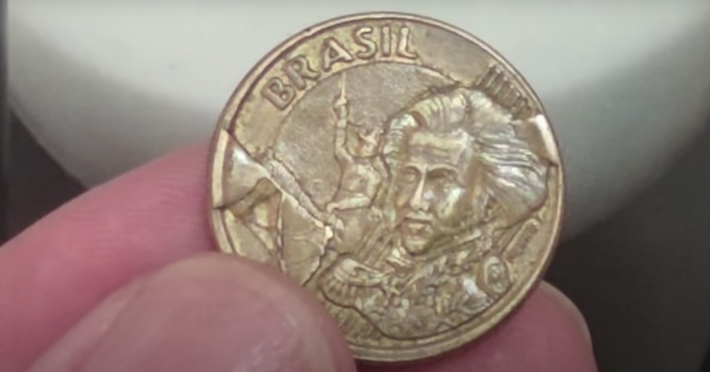 Moeda de 10 centavos com erro de cunhagem visível, segurada entre os dedos