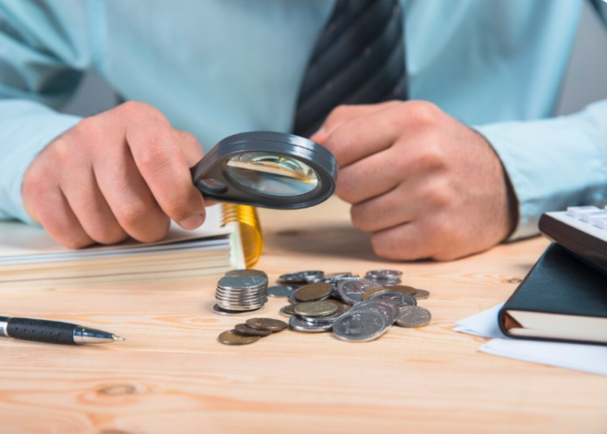 Pessoa analisando moedas com lupa para verificar autenticidade